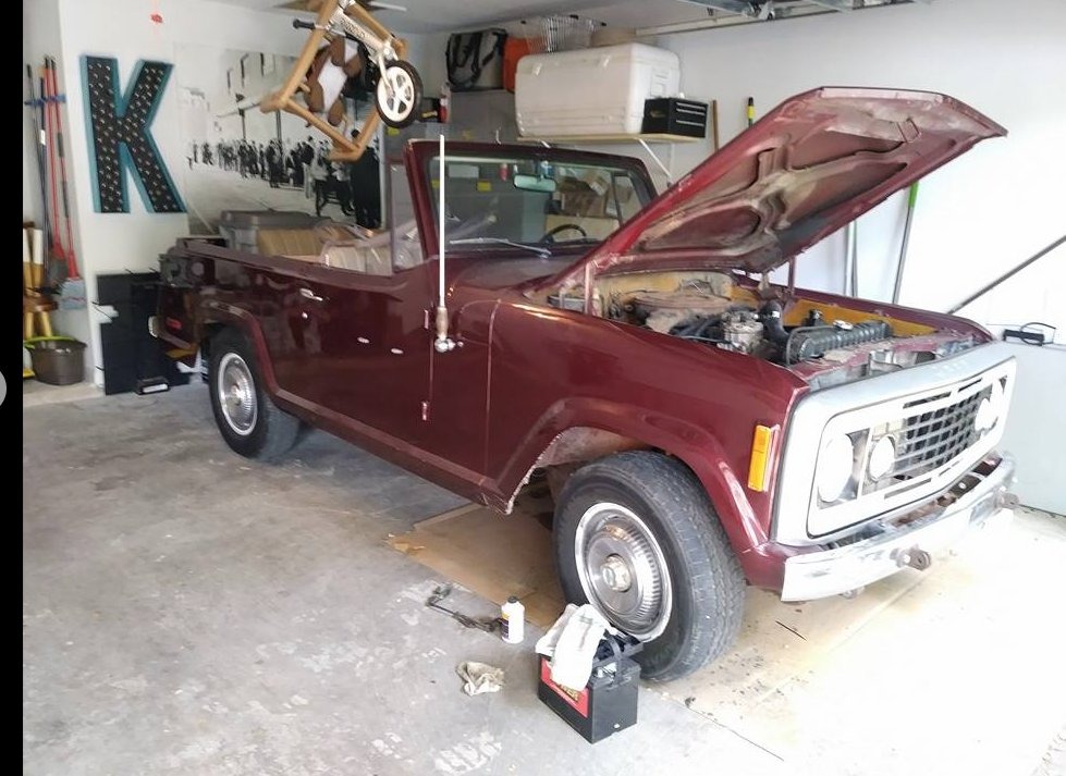 Maroon Jeepster Commando in a residential garage with the hood open, mid-repair