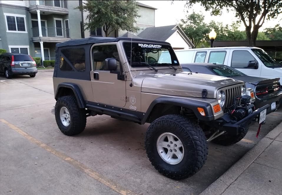 Tan Jeep TJ Wrangler with large off-road tires parked in an apartment lot